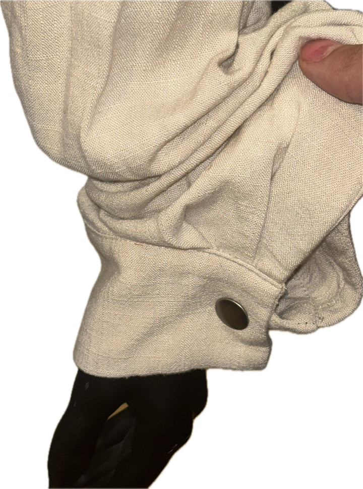 A close-up of a light beige or cream-colored textured fabric garment, possibly a sweatshirt sleeve, being held by a hand. A dark button is visible near the lower edge, and a black garment is shown underneath.